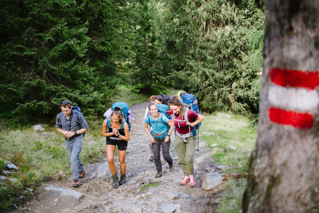 Auf dem bild sieht man drei Personen, die mit Rucksäcken wandern.